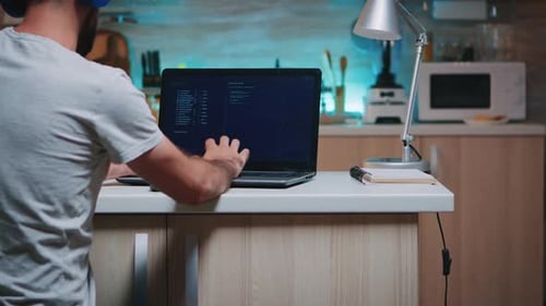 Männlicher Hacker tippt mit Headset auf Tastatur und arbeitet von zu Hause aus