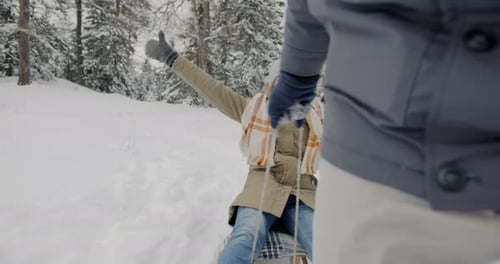 Portrait of Joyful Lady Enjoying Ride While Man Pulling Sled in Winter Forest