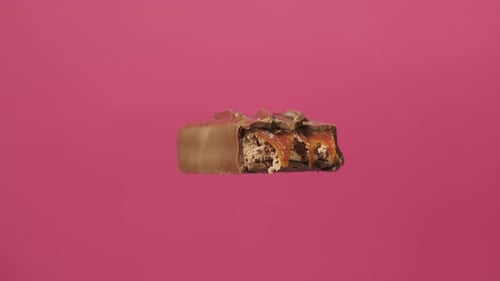A Delicious and Unhealthy Chocolate Bar Rotates on a Pink Background. Bitten Sweets Isolated. The