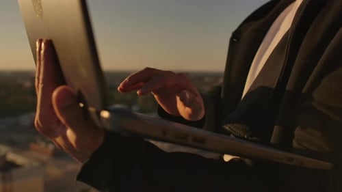 Close-up: a Programmer's Hand Typing on a Laptop Keyboard at Sunset Overlooking the Roof. A