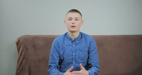 Un gars concentré en chemise bleue parle assis sur un canapé marron