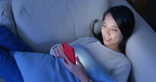 Woman use of mobile phone and lying down on sofa at home in the evening