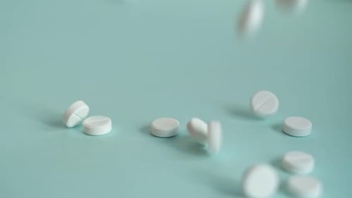 White Pills Falling on Blue Background in Slow Motion