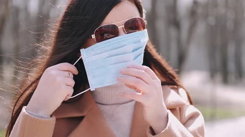Woman Putting on Surgical Face Mask Outdoors