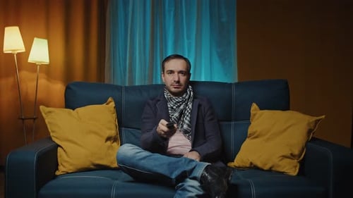 Man Relaxes on Couch, Points TV Remote