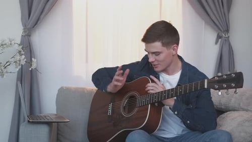 Young Man Plays Guitar at Home with Laptop
