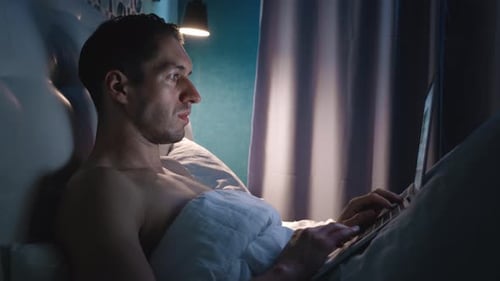 Young Man Using Laptop in Bed at Night