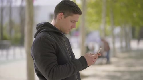 Smiling Man Uses Smartphone in Urban Park