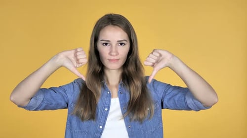 Woman Making Thumbs Down Gesture on Yellow Background