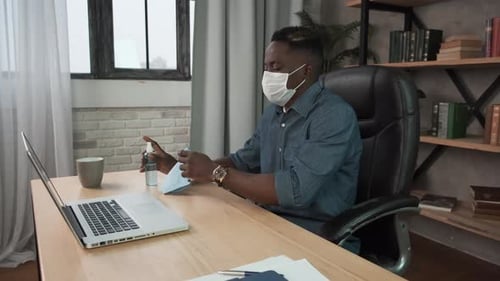 Young Adult Cleaning Laptop in Office with Mask
