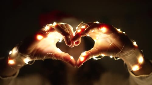 Heart Shaped Hands Holding Christmas Lights in Dark Room