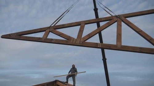 Construction Worker Guiding Truss on Roof with Pole