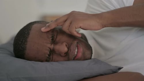 Nahaufnahme eines afrikanischen Mannes mit Kopfschmerzen beim Schlafen im Bett