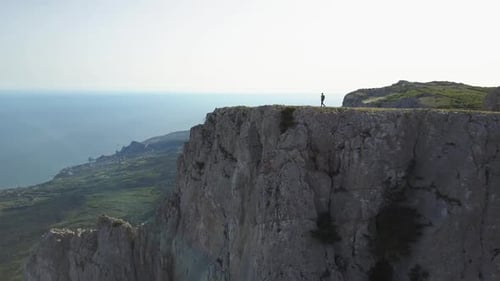 Lone Hiker on Cliff Edge Overlooking Ocean