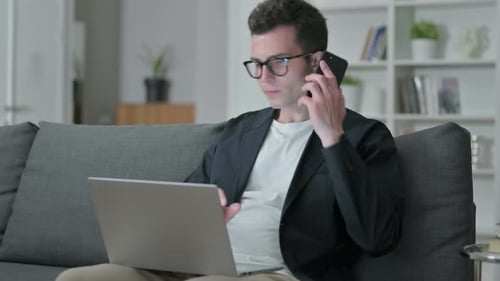 Man Working on Laptop and Talking on Phone