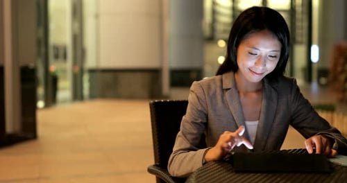 Woman Works on Tablet Computer at Outdoor Cafe at Night