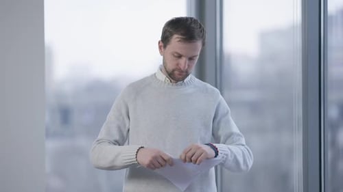 Sad Man Tearing Paper and Looking Out the Window in Office