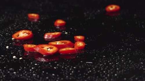 Glühende Chilischoten, die auf feuchte schwarze Oberfläche fallen