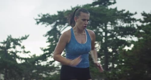 A Tracking Shot of a Young Woman in Sportswear Jogging Through an Evergreen Forest on a Country Road