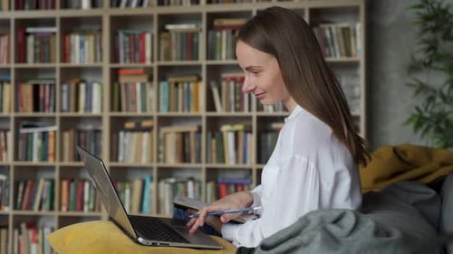 Woman Working on Laptop and Writing in Notebook