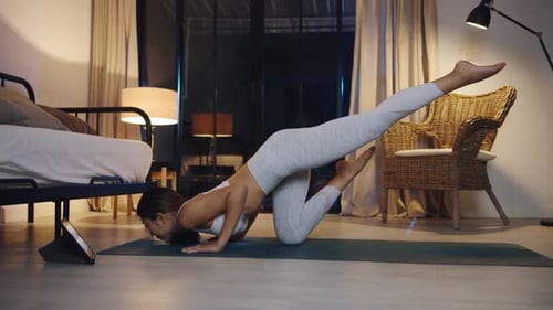 Una mujer asiática hace ejercicio y usa una tableta para ver un vídeo tutorial de yoga en casa por la noche.