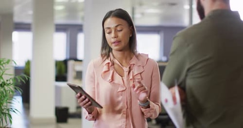 Video of diverse businesswoman and businessman using tablet and talking in office