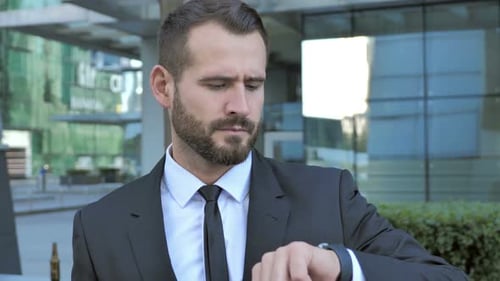 Bearded Businessman Checking Watch Outside Office Building
