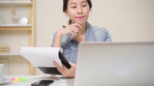 Woman Reviews Papers While Working on Laptop