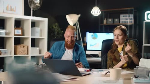 Joyeux jeune homme et femme célébrant la victoire avec un ordinateur portable au bureau.