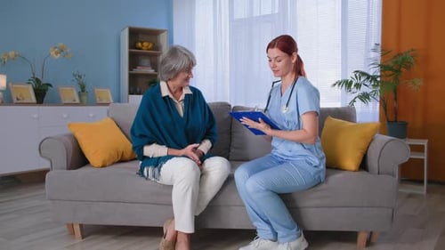 Medical Examination at Home Female Doctor in Uniform with Clipboard Consulting Elder Woman Patient