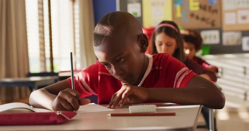 Focused Boy Writing in Classroom at School Desk