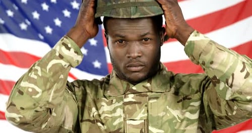 Soldier Puts on Helmet in Front of Flag