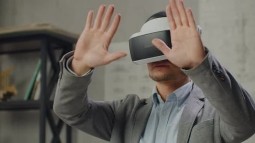 Modern Man Engineerdesigner in the Office with Large Windows Stands in a Virtual Reality Helmet Uses