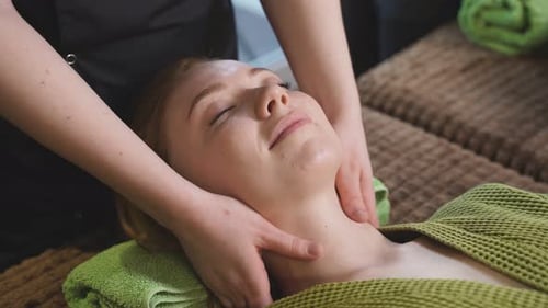 Ruhige Frau liegt im Spa-Salon auf dem Bett und wird an Hals und Brust massiert