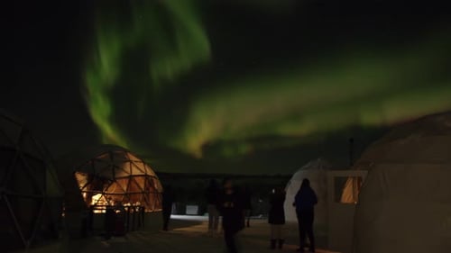 A Group of Tourists Next to Glass Igloos are Filming the Swirls of the Aurora Borealis on Their