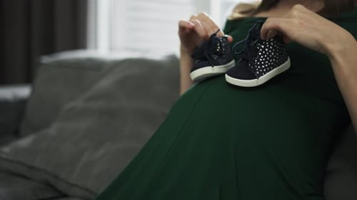 Pregnant Woman Holding Baby Shoes on Her Belly