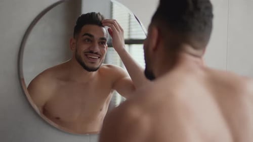 Attractive Man Styling Hair in Mirror Reflection