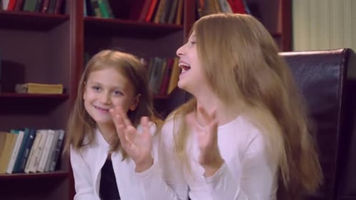 Two Young Girls Smiling in Front of Bookshelf