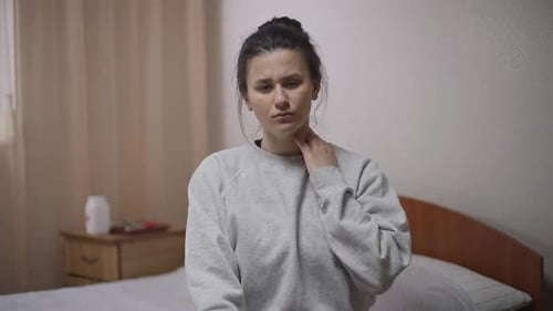 Woman Sitting in Bedroom with Neck Pain