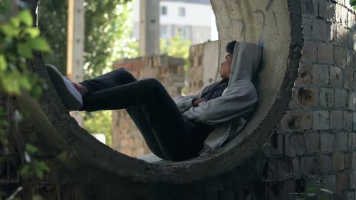 Trauriger einsamer Student im Kapuzenpullover, allein sitzend, verlassenes Gebäude