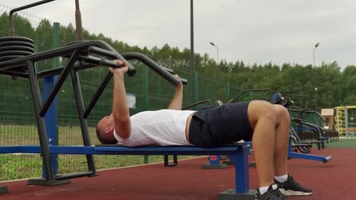 Young Male Athlete on a Simulator Trains His Pectoral Muscles in the Outdoors
