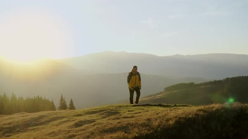 Man Hiking on Hilltop at Sunrise with Mountains