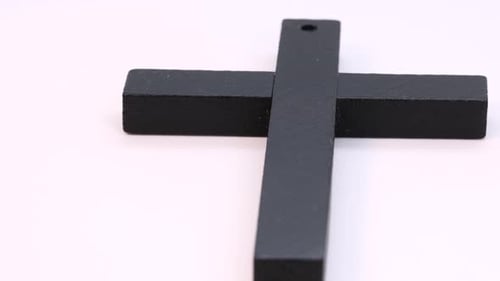 Homemade black wooden cross rotating on white surface. Macro shot, close view in 4k of christian hol