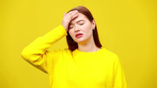 Worried Woman Holding Forehead Against Yellow Background
