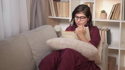 Young Woman Reading a Book on Couch Indoors