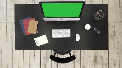 Office desk with computer and screen seen to camera. Green