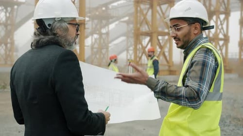 Back View of Engineers Discussing Construction Project Looking at Blueprint