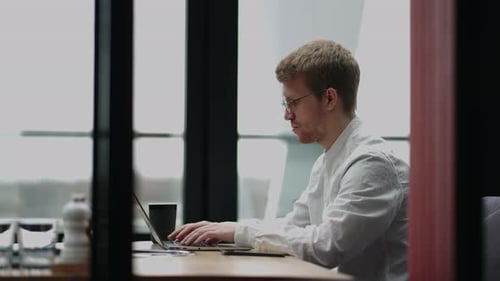 Young Man Wearing Glasses and Smiling As He Works on His Laptop to Get All His Business Done Early