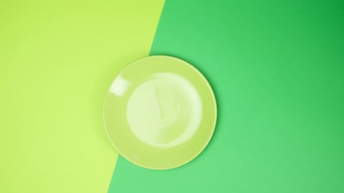two female hands put on a green surface a round ceramic plate forks with a knife
