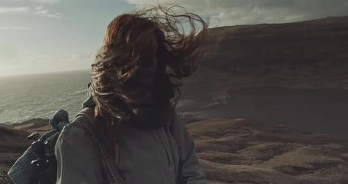 Girl Stands on Rocky Coastline with Wind